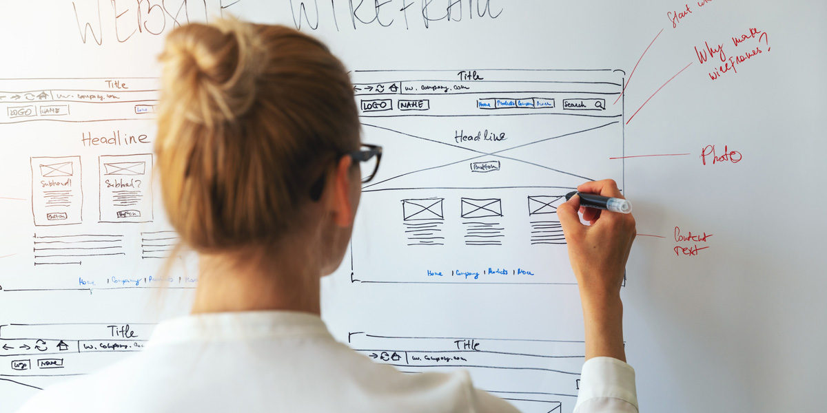 A person trying to learn UX design, standing at a whiteboard, drawing wireframes 